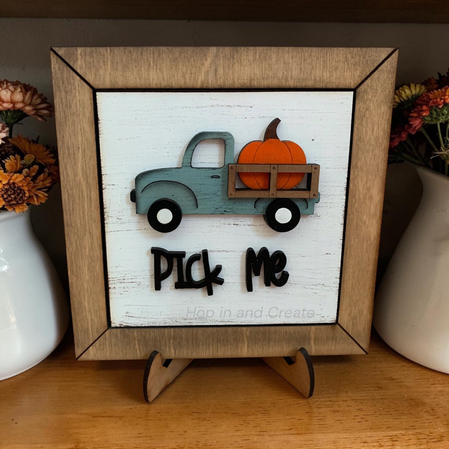 Decorative sign with a truck and pumpkin design on a stand, framed in wood.