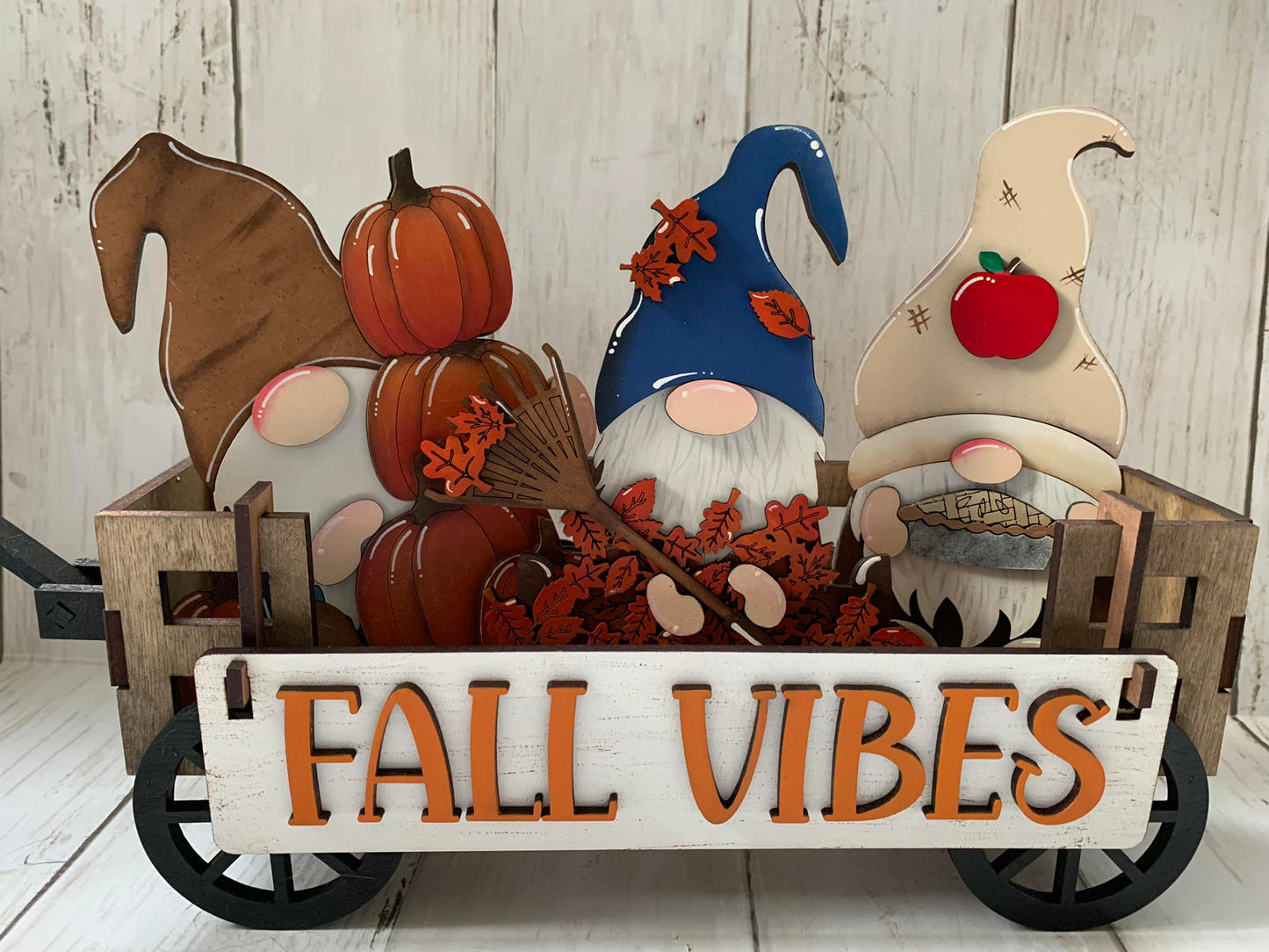 A decorative gnome crate with a 'FALL VIBES' sign, featuring gnomes, pumpkins, and autumn leaves in a rustic wagon.