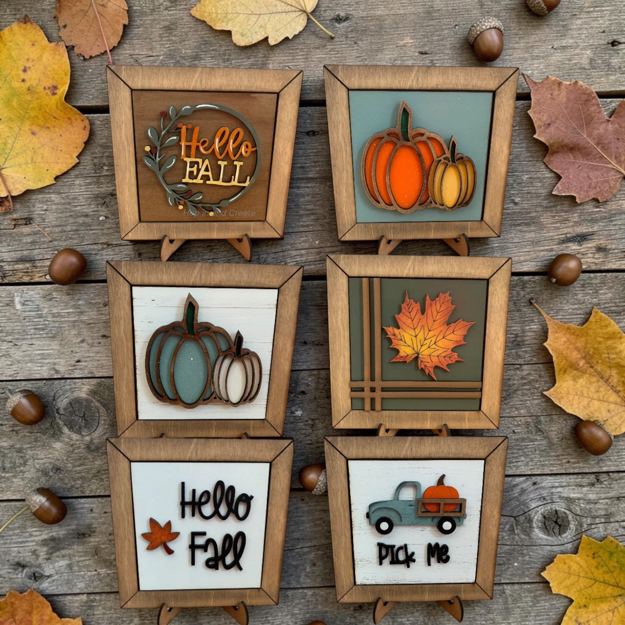 Set of autumn-themed decorative signs on a wooden surface with leaves and acorns.
