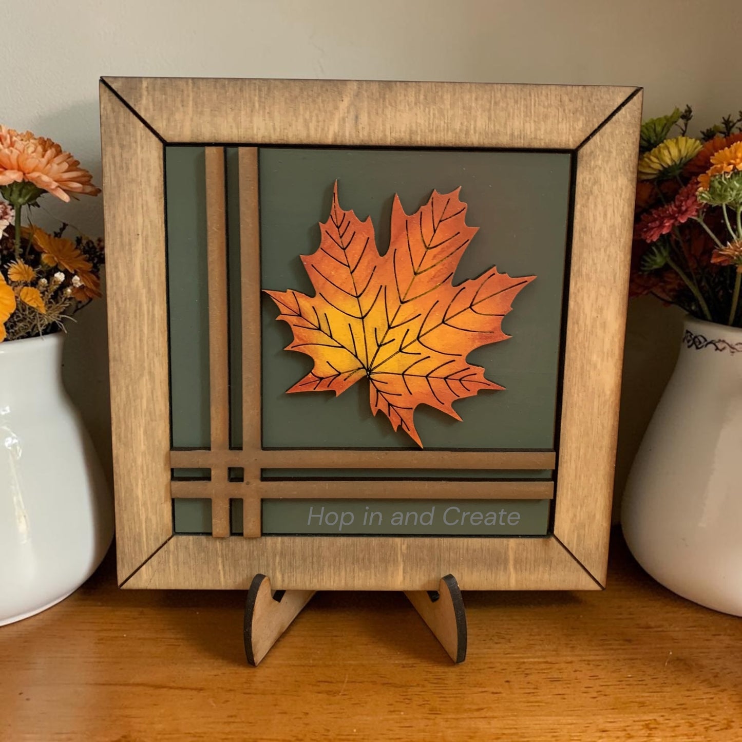 Decorative frame with a leaf design on a wooden surface with flowers in the background.