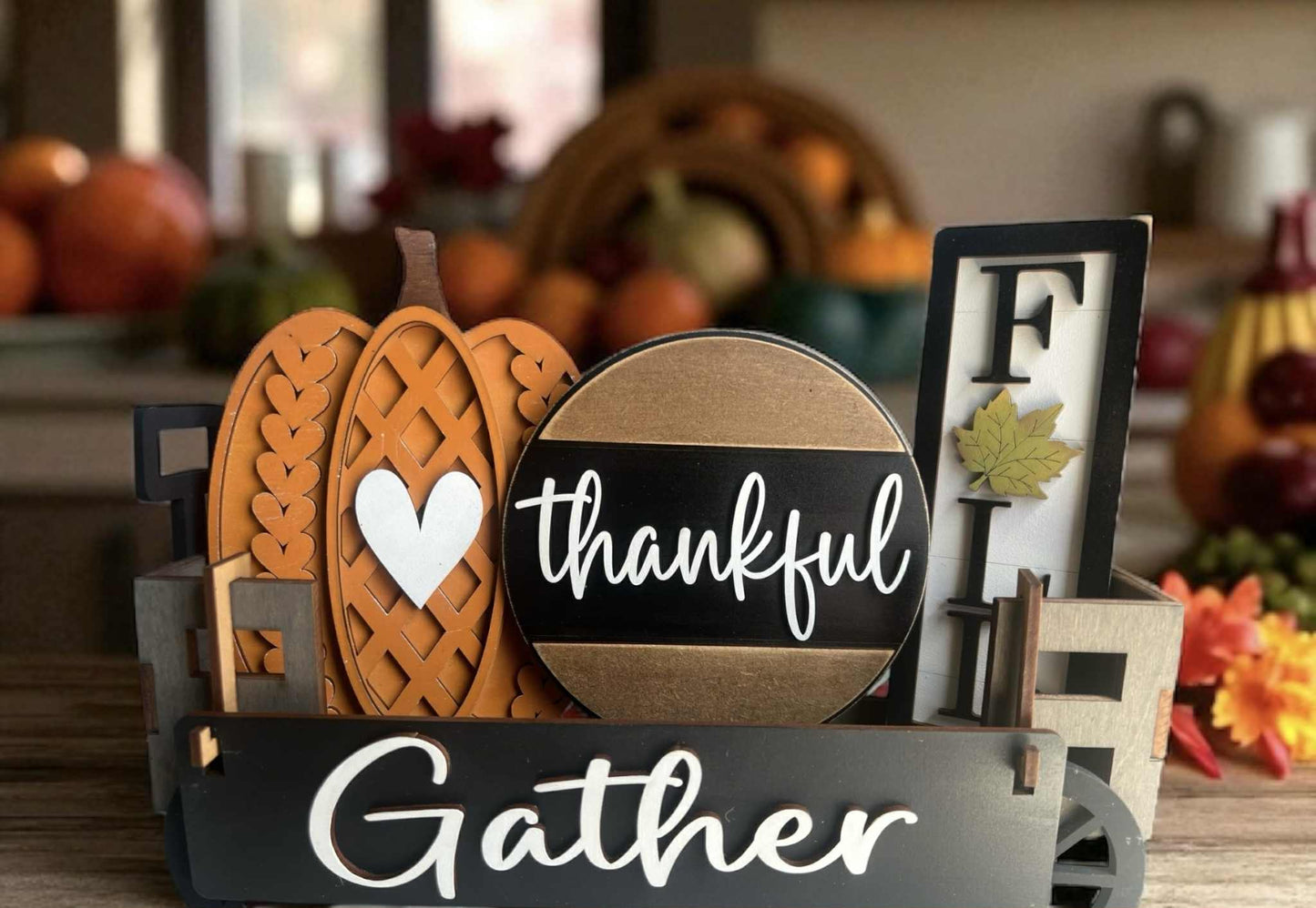 Decorative sign with pumpkins and 'thankful' and 'gather' text in a fall-themed setting.