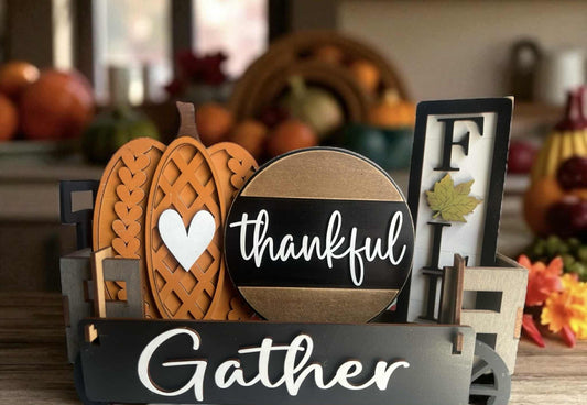Decorative sign with pumpkins and 'thankful' and 'gather' text in a fall-themed setting.