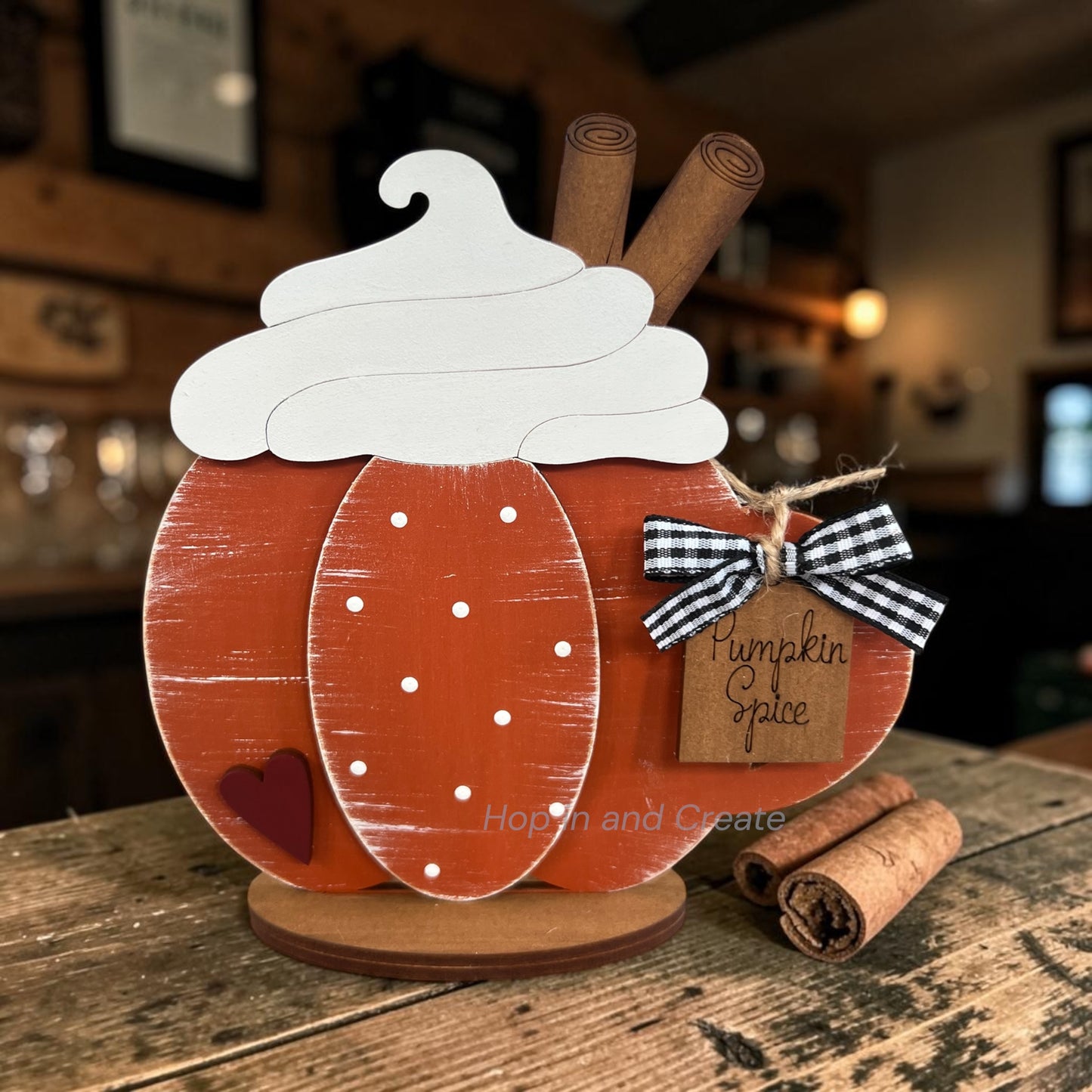Decorative pumpkin with whipped cream, cinnamon sticks, and a tag on a wooden surface.