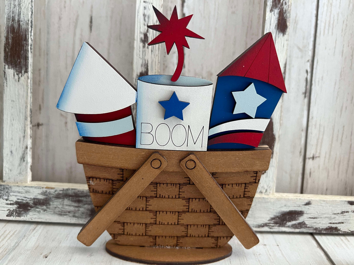 A decorative basket with interchangeable inserts themed as fire crackers, with red, white, and blue colors and the word 'BOOM' displayed.