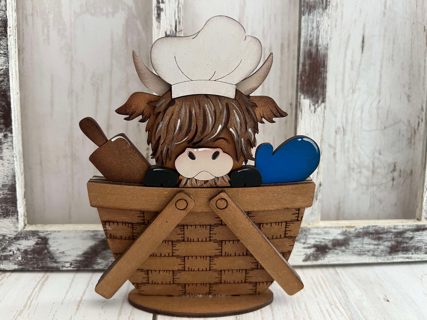 A decorative mini basket insert with a highland cow wearing a chef's hat and holding a rolling pin and an oven mitt