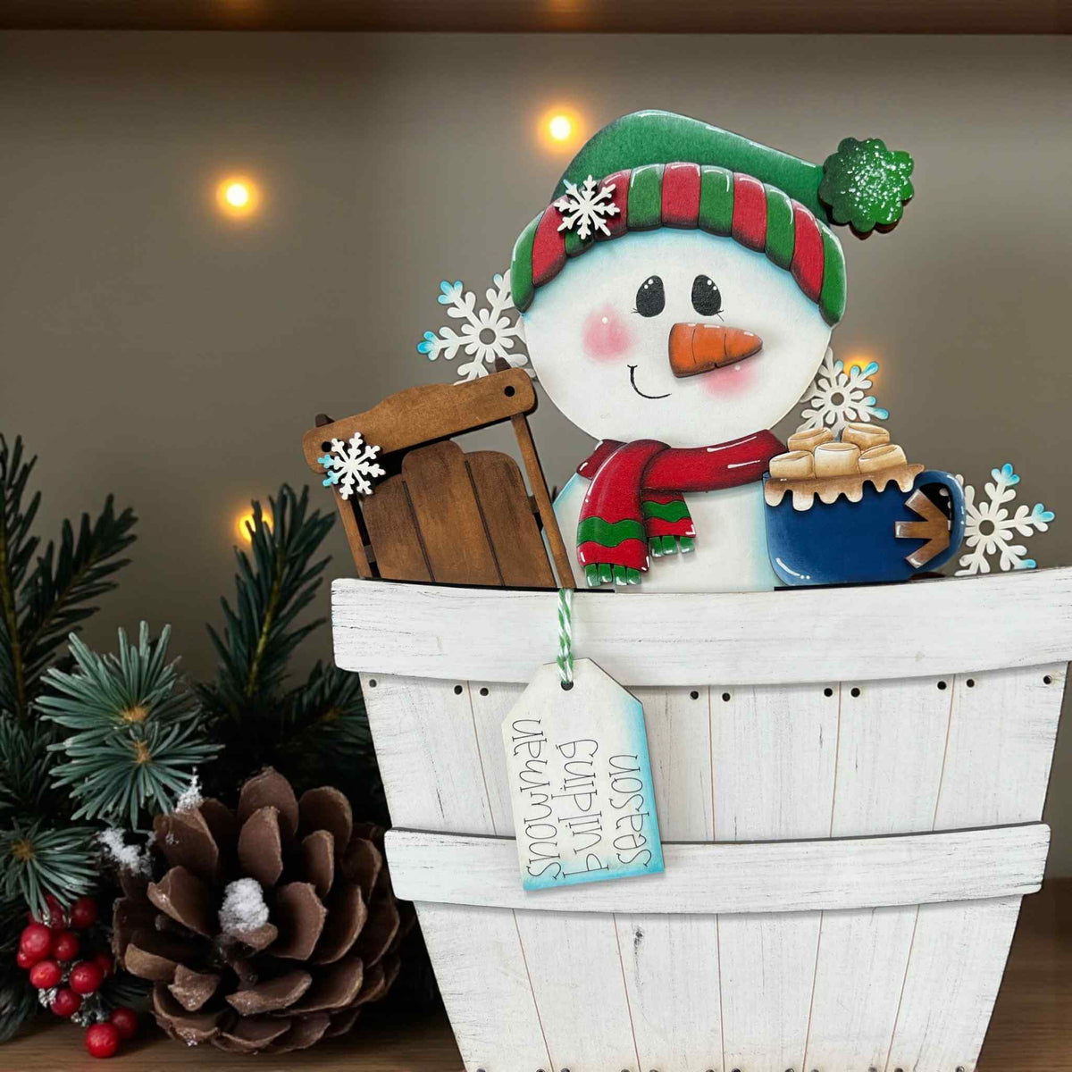 Decorative snowman with a sleigh, surrounded by Christmas decorations on a wooden surface.